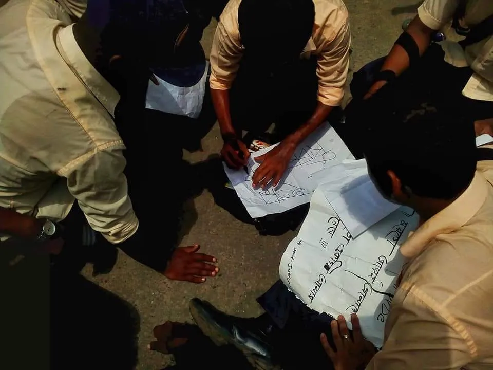 Students sitting on the street pavement writing hand-drawn placards and safety guidelines